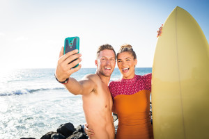 Male and female couple with a surf board taking a selfie next to the ocean